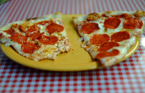 Two slices of pepperoni pizza on a yellow plate, resting on a red and white checkered tablecloth.