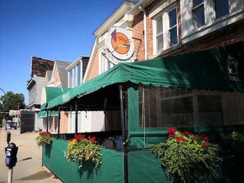 Exterior of a restaurant with a green awning, flower boxes, and a sign featuring a bird logo on a sunny day.