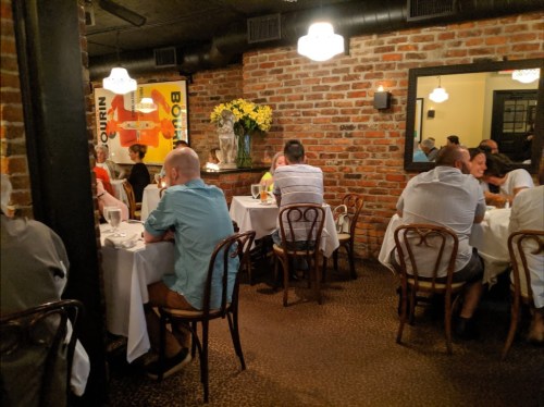 Cozy restaurant interior with brick walls, tables set for dining, and patrons enjoying their meals in a warm atmosphere.