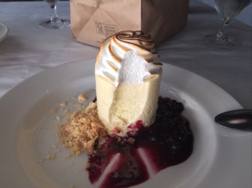 A slice of creamy dessert topped with meringue, served on a plate with berry sauce and crumbled topping.