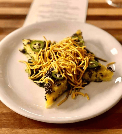 A plate of triangular polenta topped with green herbs, sliced jalapeños, and crispy noodles.