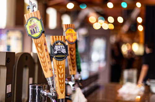 Close-up of beer taps with colorful labels in a bar, blurred lights in the background.