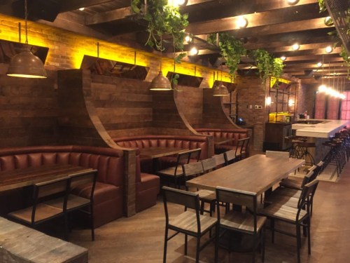 Cozy restaurant interior with wooden decor, leather seating, and warm lighting, featuring tables and a bar area.