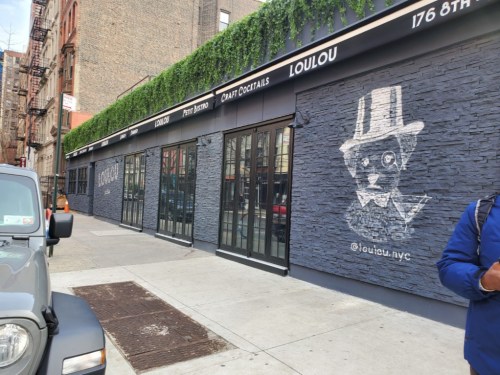 Exterior of Loulou restaurant featuring a stone wall with a whimsical cat illustration and large glass windows.