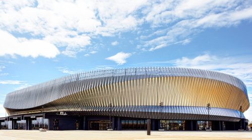 A modern, wavy building with a metallic facade under a blue sky with scattered clouds.