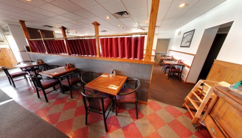Interior of a restaurant featuring wooden tables, black chairs, and red curtains, with a checkered floor design.