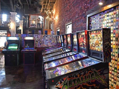 A vibrant arcade with multiple pinball machines and colorful wall decor in a rustic brick setting.