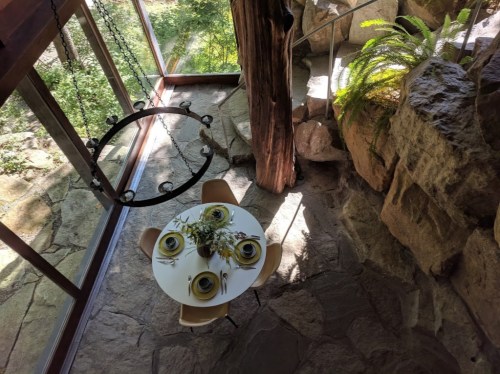 A cozy dining area with a round table set for four, surrounded by natural stone and greenery.