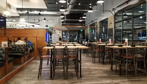 Interior of a modern restaurant with empty tables, chairs, and a few patrons in the background. Bright and spacious atmosphere.