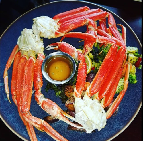 A plate of crab legs served with a small bowl of dipping sauce and a side of mixed vegetables.