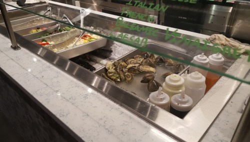 A seafood display with oysters, sauces, and a variety of salads in a restaurant setting.