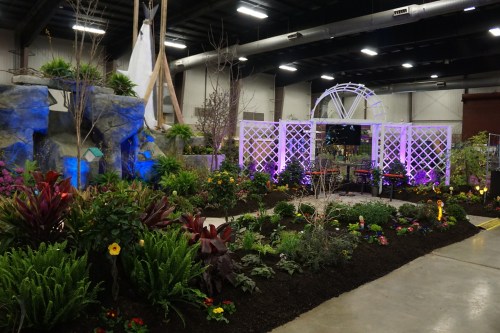 A vibrant indoor garden display featuring colorful plants, a white trellis, and decorative rocks under soft lighting.