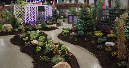 A landscaped garden path with colorful plants, rocks, and decorative features in a well-lit indoor setting.