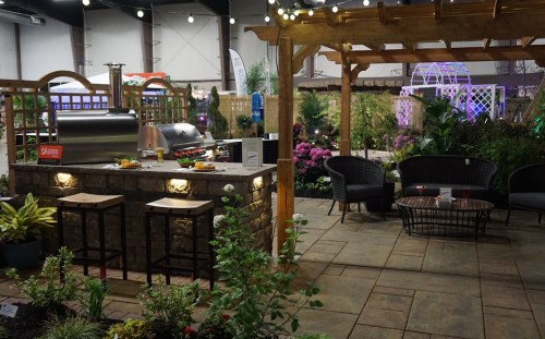 A cozy outdoor space featuring a stone grill, seating area, and lush plants under decorative lighting.