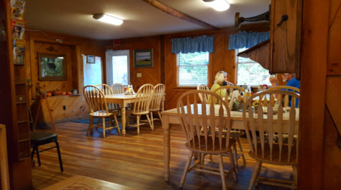 Cozy dining area with wooden tables and chairs, featuring rustic decor and natural light from windows.