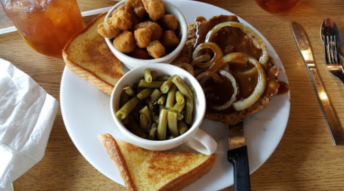 A plate with fried chicken topped with onions, green beans, fried okra, and toast, accompanied by a drink.