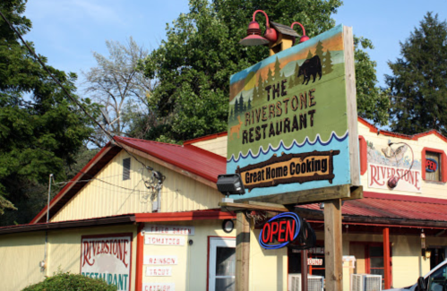 Sign for The Riverstone Restaurant featuring "Great Home Cooking," with an open neon sign and a rustic exterior.