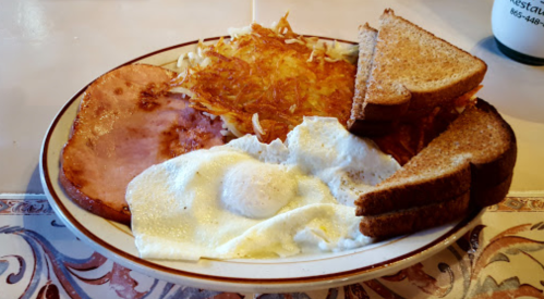 A plate of breakfast featuring eggs, ham, hash browns, and two slices of toasted bread.
