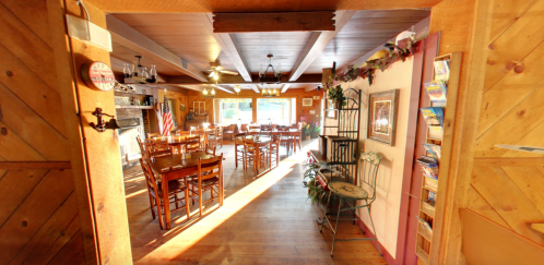 Cozy restaurant interior with wooden decor, tables, and sunlight streaming through large windows.