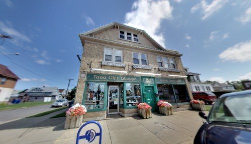 A brick building with a green storefront, "Tara Gift Shoppe," adorned with flower planters and a clear blue sky.