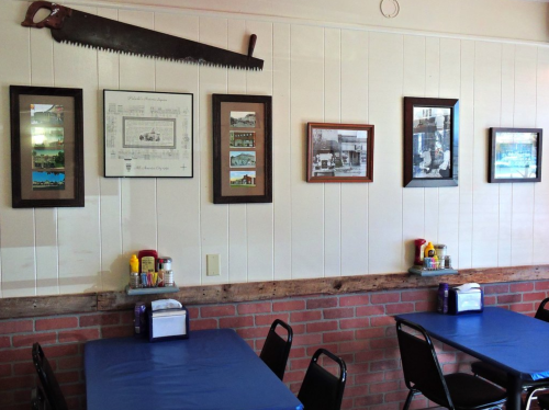 A cozy restaurant interior with blue tables, black chairs, and framed photos on the wall, featuring a large saw above.