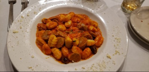 A plate of gnocchi in a rich tomato sauce, garnished with herbs and sprinkled with cheese.