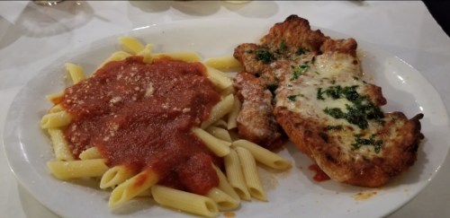 A plate of pasta with marinara sauce and a breaded chicken cutlet topped with cheese and herbs.