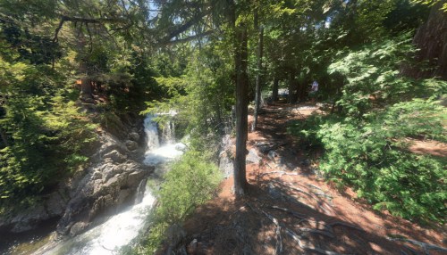 A scenic view of a waterfall surrounded by lush green trees and rocky terrain on a sunny day.