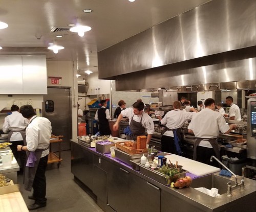 A busy restaurant kitchen with chefs preparing dishes, working at stations, and focused on their tasks.