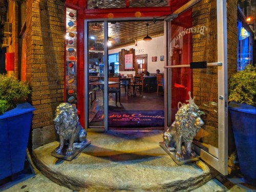 Entrance of a restaurant featuring two silver lion statues and a glimpse of the interior with wooden tables.
