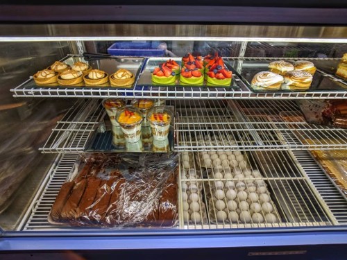 A display case filled with desserts, including cakes, pastries, and cups of layered treats, alongside a tray of eggs.