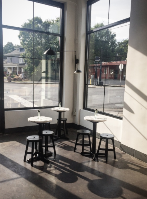 A bright café interior with marble-topped tables and black stools, featuring large windows and soft shadows.