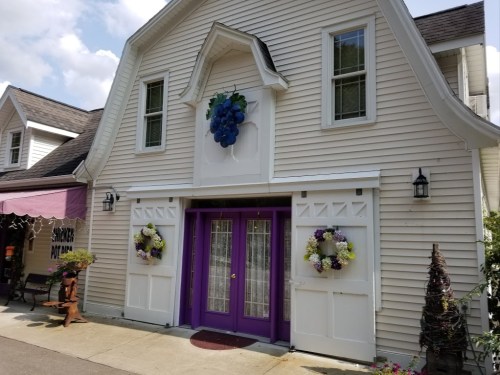 A charming white building with purple doors, adorned with grape-themed decor and floral wreaths on either side.