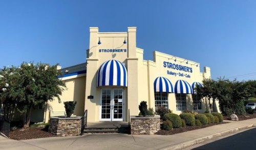 Exterior of Strossner's Bakery, Deli & Café, featuring blue and white striped awnings and a sunny sky.