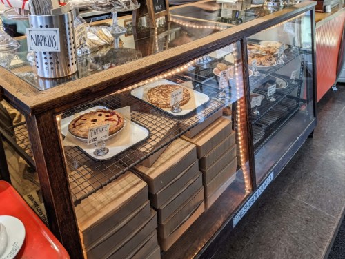 A display case filled with various pies and dessert boxes in a cozy café setting.