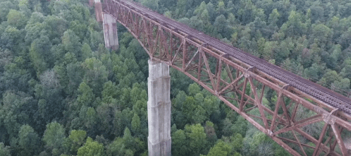 Aerial view of a rusted railway bridge spanning over dense green trees.