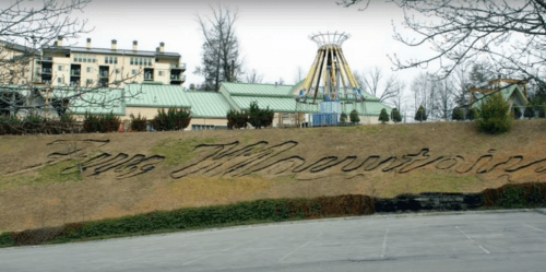 A hillside with the words "Zia Mheventain" carved into it, overlooking an amusement park with rides in the background.