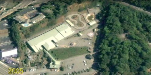 Aerial view of an amusement park in 2005, featuring rides and a parking lot surrounded by trees.
