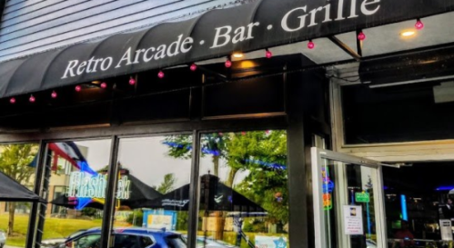 Exterior of a retro arcade bar and grille with a black awning and colorful signage.