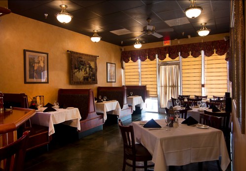 Cozy restaurant interior with tables set for dining, featuring booths, warm lighting, and elegant decor.