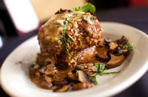 A savory meat dish topped with melted cheese, served on a bed of sautéed mushrooms and garnished with herbs.