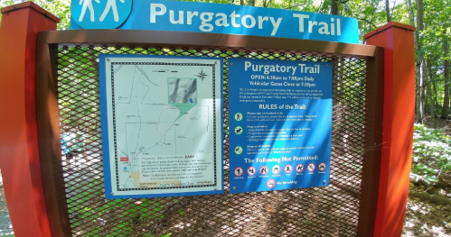 Sign for Purgatory Trail with rules and map, surrounded by trees, indicating trail hours and regulations.