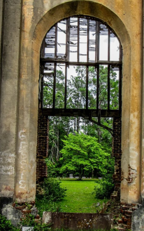 View through an arched window of a ruined building, revealing a lush green landscape beyond.