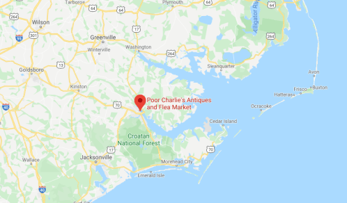 Map showing the location of Poor Charlie's Antiques and Flea Market near the coast, surrounded by green areas and water.