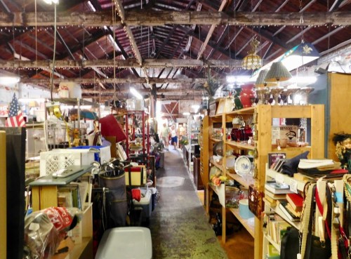 A bustling antique shop aisle filled with various vintage items and wooden shelves, under a rustic ceiling.
