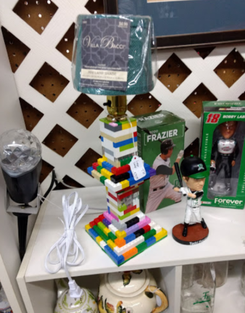 A colorful lamp made of building blocks, with a shade on top, next to a baseball figurine and a light bulb.