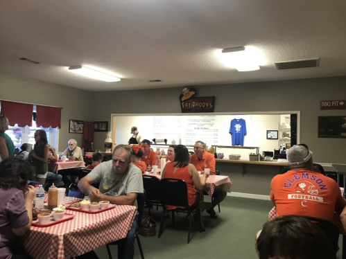 A cozy restaurant interior with patrons dining at tables, a menu board in the background, and a BBQ theme.