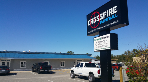 Sign for Crossfire Paintball, North Carolina's only indoor paintball park, with a clear blue sky in the background.