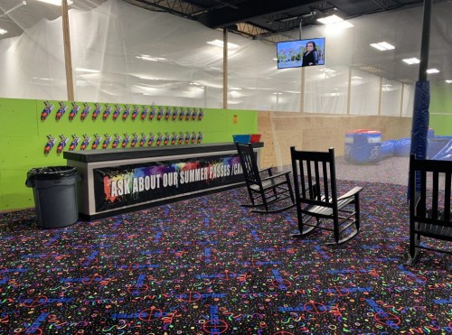 A colorful indoor space with a patterned carpet, a counter, rocking chairs, and a TV on the wall.