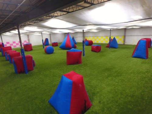 Indoor paintball arena featuring various inflatable obstacles in red and blue on a green turf floor.